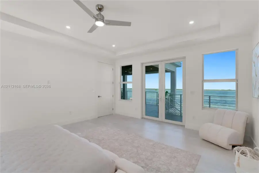 Tray ceiling with brushed nickel ceiling fan, wood-finish flooring, double-glass French doors, and waterfront exterior balcony Tray ceiling with brushed nickel ceiling fan, wood-finish flooring, double-glass French doors, and waterfront exterior balcony