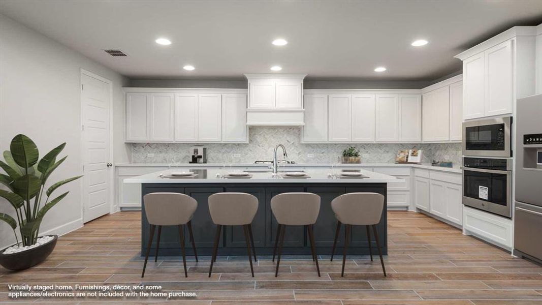 Kitchen with appliances with stainless steel finishes, light hardwood / wood-style floors, white cabinets, decorative backsplash, and a center island with sink