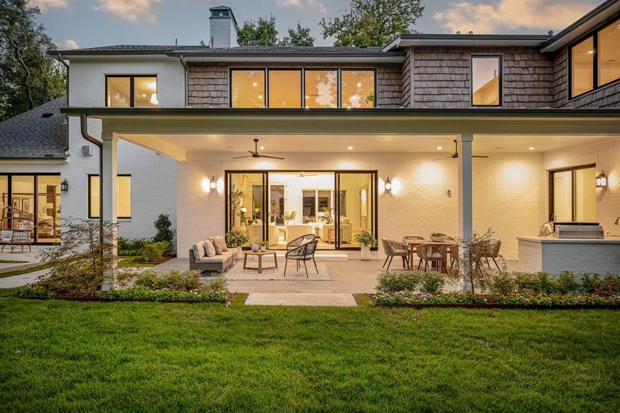 Back house at dusk with ceiling fan, an outdoor living space, a lawn, and a patio