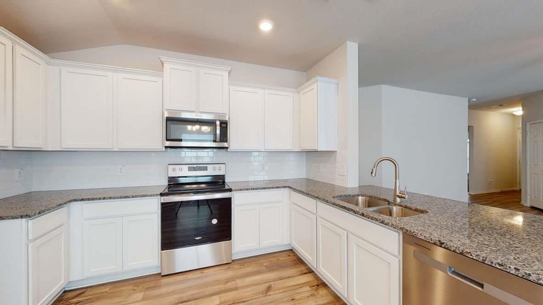 Kitchen with stainless steel appliances, light wood-style flooring, dark stone counters, white cabinets, and recessed lighting