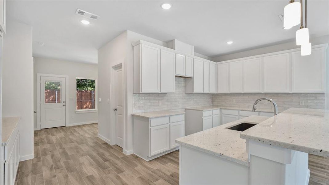 Kitchen with light wood-type flooring, sink, decorative light fixtures, white cabinetry, and light stone countertops