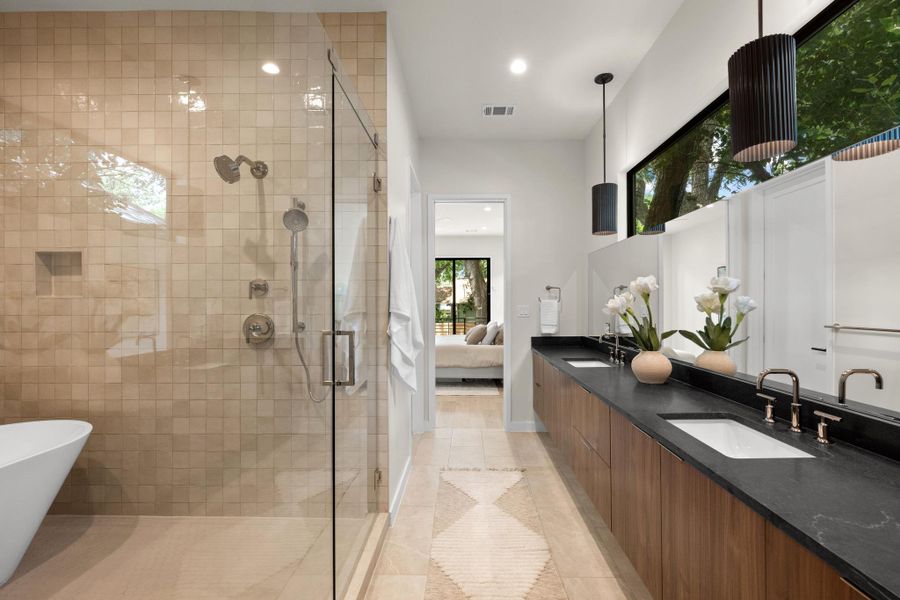 A spacious primary bathroom boasts a dual vanity, sleek dark countertops, and an inviting walk-in shower. A spacious primary bathroom boasts a dual vanity, sleek dark countertops, and an inviting walk-in shower.