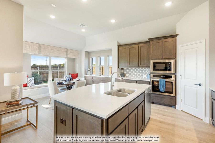 Kitchen with large center island, sink, dark wood cabinets, stainless steel appliances, and light hardwood floors Kitchen with large center island, sink, dark wood cabinets, stainless steel appliances, and light hardwood floors