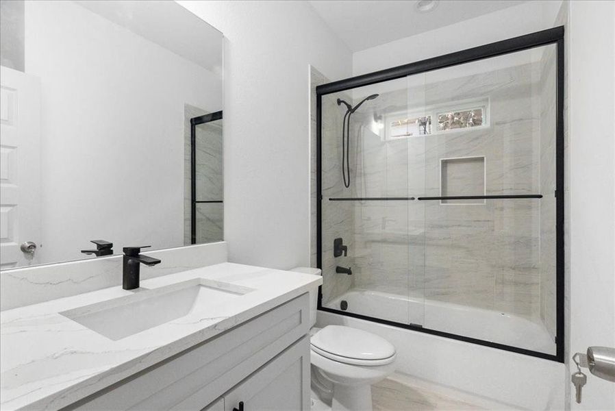 Full bathroom with shower / bath combination with glass door, vanity, and toilet