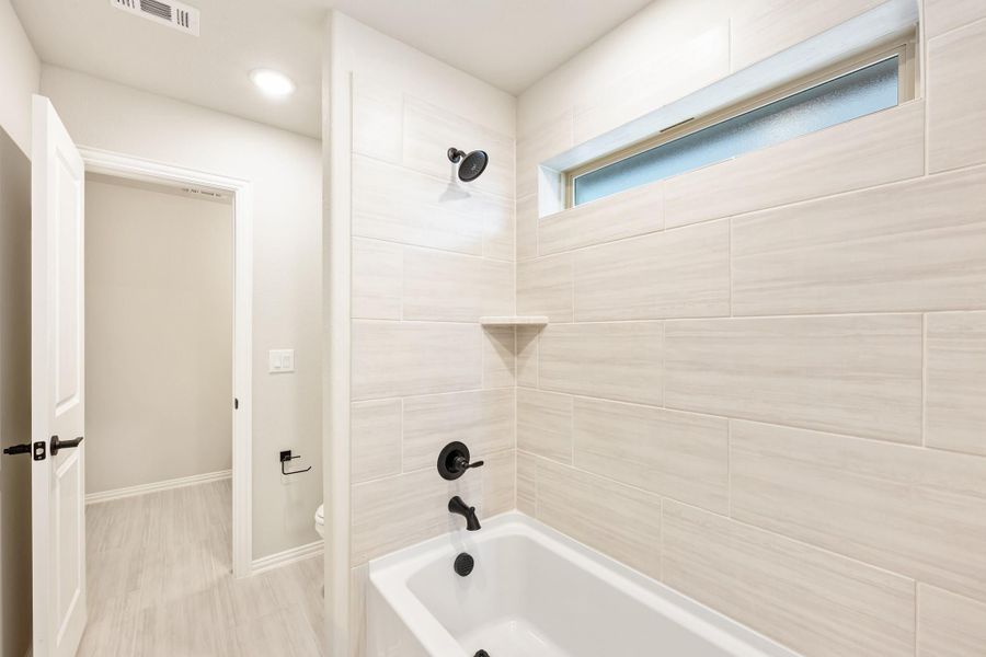 Bathroom with soaking tub, tiled shower surround, black fixtures, and small privacy window above the tub Bathroom with soaking tub, tiled shower surround, black fixtures, and small privacy window above the tub