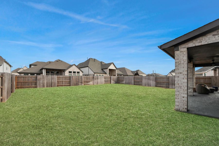 Spacious fenced backyard with covered patio and open lawn.