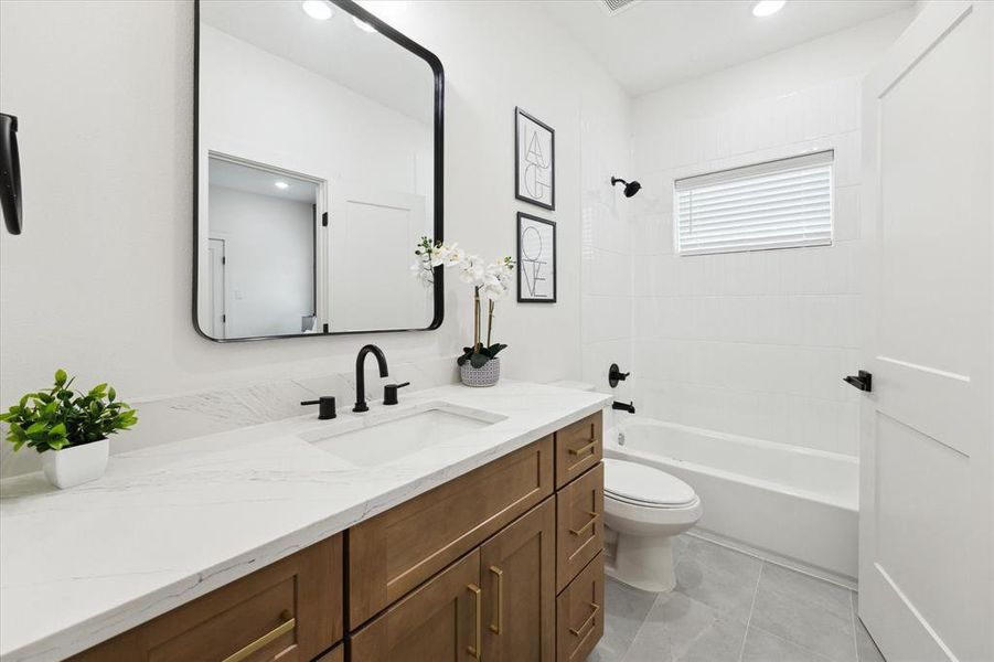 This stylish shared bath showcases elegant finishes throughout. A spacious vanity with an under-mount sink and added storage is topped with white quartz and accented by dark hardware, while the tub and shower combo is framed by classic white subway tiles, creating a clean and timeless look.