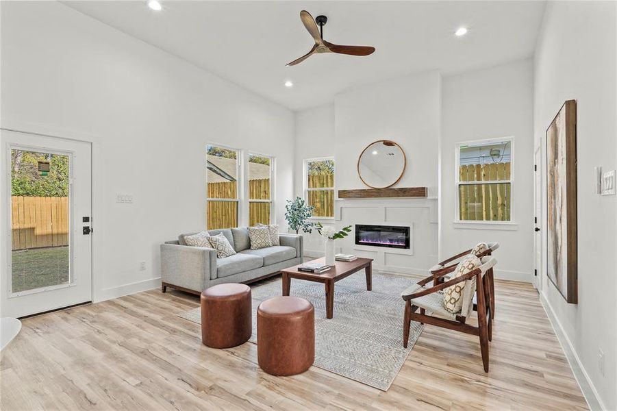 Living area featuring recessed lighting, light wood-style floors, a glass covered fireplace, ceiling fan, and a towering ceiling