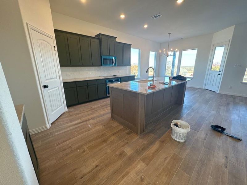Kitchen featuring dark wood finished floors, an island with sink, pendant lighting, a chandelier, and appliances with stainless steel finishes Kitchen featuring dark wood finished floors, an island with sink, pendant lighting, a chandelier, and appliances with stainless steel finishes