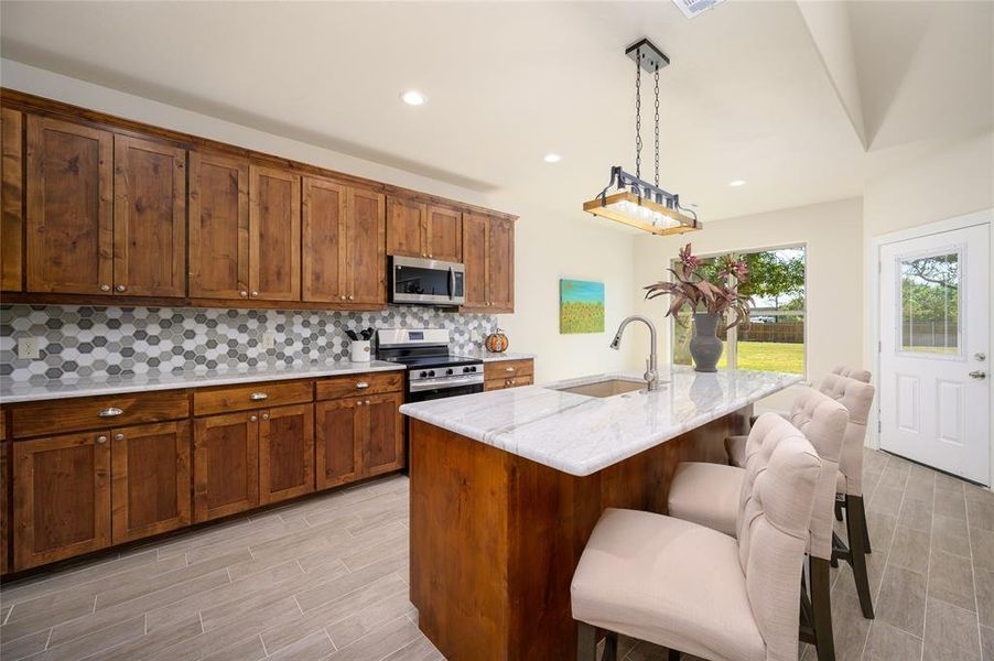 Kitchen featuring a kitchen island with sink, stainless steel appliances, sink, a kitchen bar, and decorative light fixtures