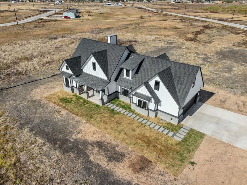 A newly constructed modern farmhouse with a dark shingle roof and a concrete driveway awaits its finishing touches. A newly constructed modern farmhouse with a dark shingle roof and a concrete driveway awaits its finishing touches.