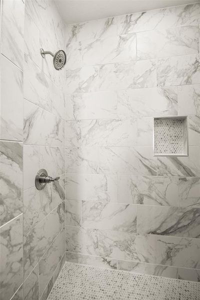 Shower featuring large format marble-look wall tiles and a pebble-finish floor