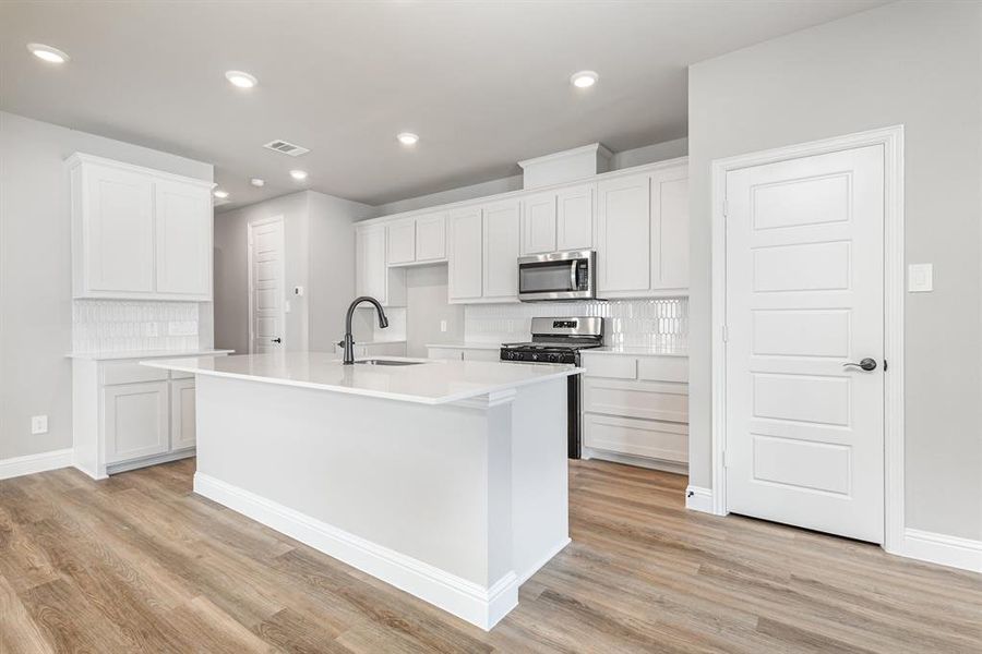Kitchen with backsplash, white cabinetry, appliances with stainless steel finishes, a kitchen island with sink, and light wood-style flooring