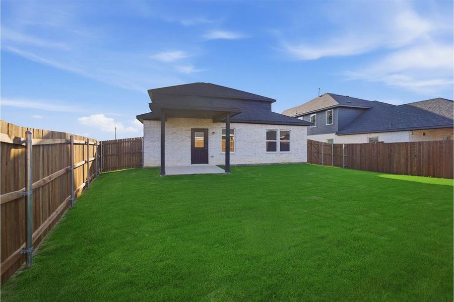 Spacious backyard featuring a lush green lawn, full privacy fencing, and a covered concrete patio