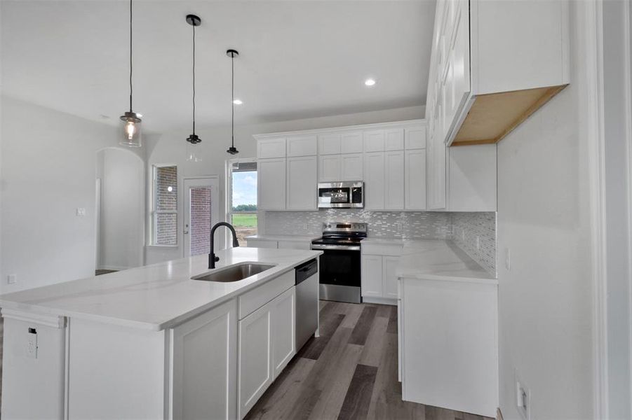 Kitchen with an island with sink, stainless steel appliances, white cabinets, and decorative light fixtures