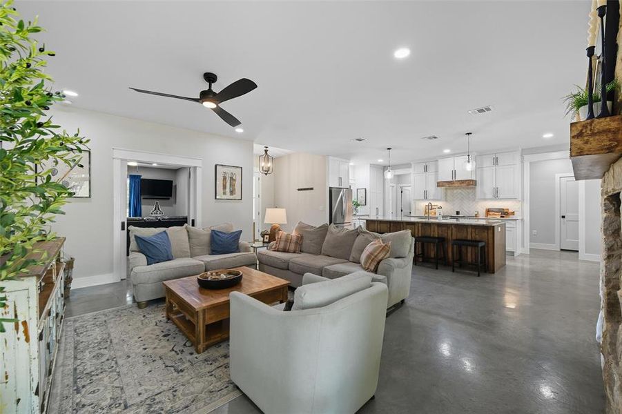 Living room with concrete floors, recessed lighting, ceiling fan, and a chandelier Living room with concrete floors, recessed lighting, ceiling fan, and a chandelier