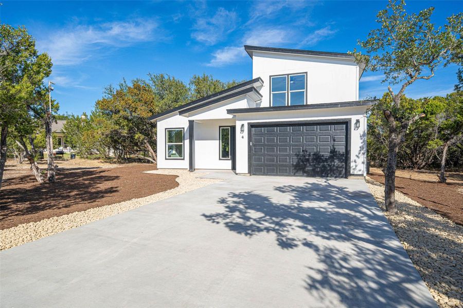 The property features a modern white exterior with black trim, a dark gray garage door, and a concrete driveway