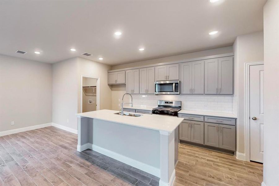 Kitchen with sink, light hardwood / wood-style floors, a center island with sink, and appliances with stainless steel finishes