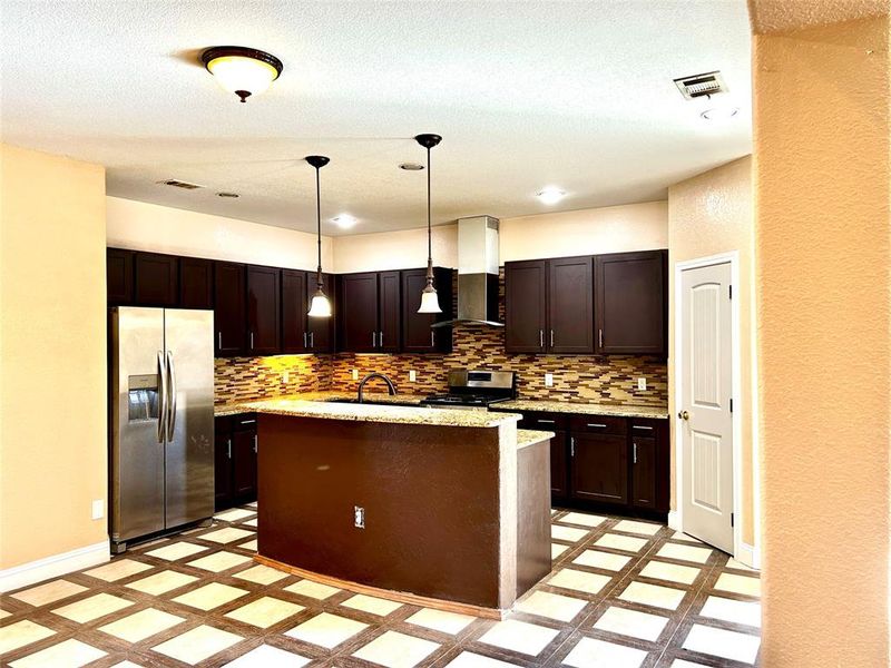 Kitchen featuring backsplash, stainless steel appliances, extractor fan, decorative light fixtures, and an island with sink