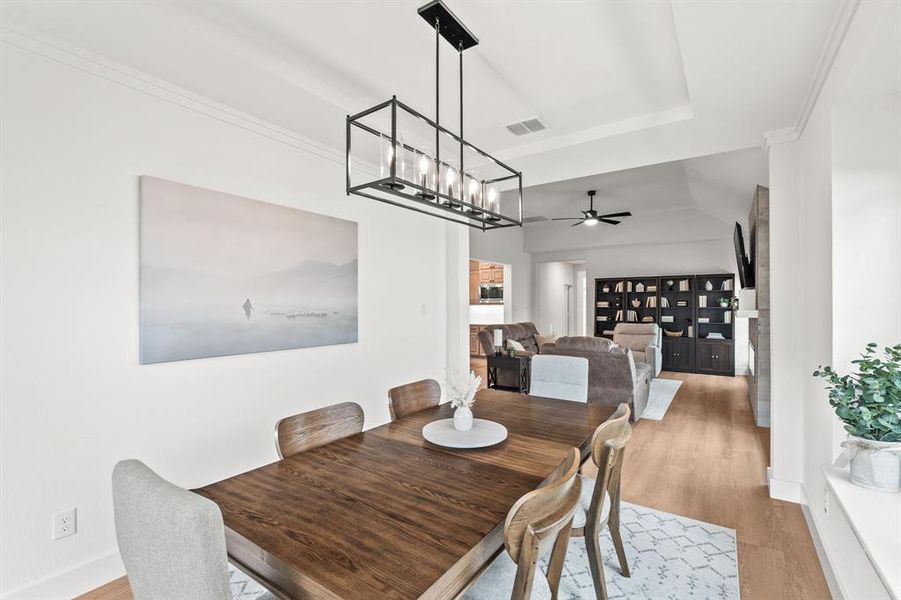 Dining room featuring light wood finished floors, ceiling fan, a raised ceiling, and ornamental molding Dining room featuring light wood finished floors, ceiling fan, a raised ceiling, and ornamental molding