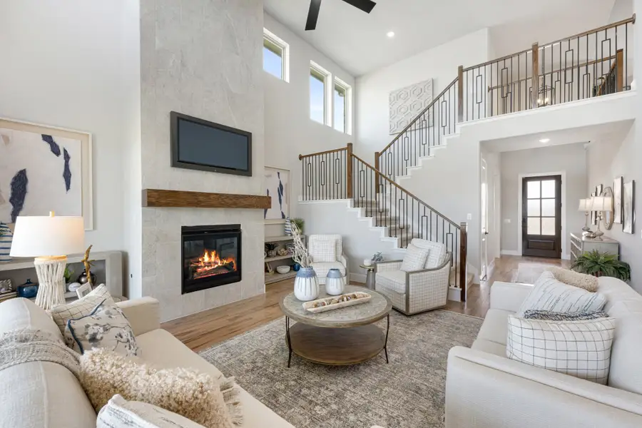 Open living room with two-story ceiling, stone fireplace, and staircase with metal railings