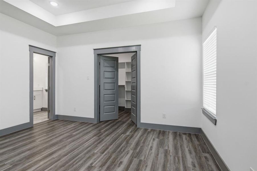Spacious room featuring wood-finish flooring, white walls, and a tray ceiling with recessed lighting
