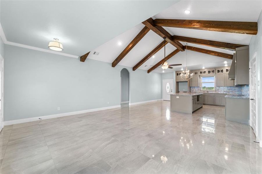 Unfurnished living room featuring beam ceiling, ceiling fan with notable chandelier, light tile patterned floors, and high vaulted ceiling