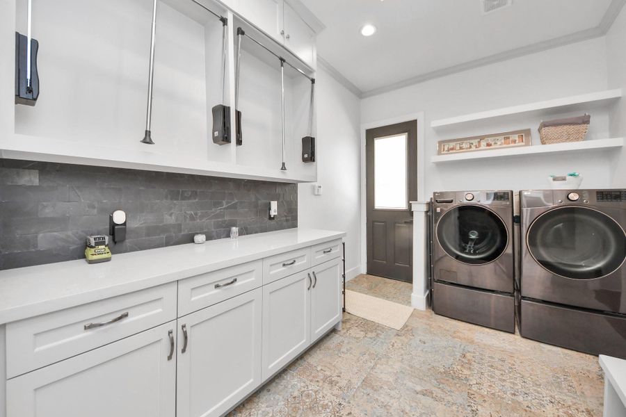 This photo showcases a modern laundry room featuring sleek white cabinetry, ample counter space, and dark appliances. There is a door leading outside and open shelving for storage, creating a functional and organized space.