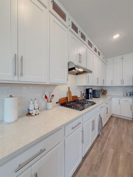 Kitchen featuring under cabinet range hood, white cabinets, light wood-type flooring, glass insert cabinets, and stainless steel gas stovetop