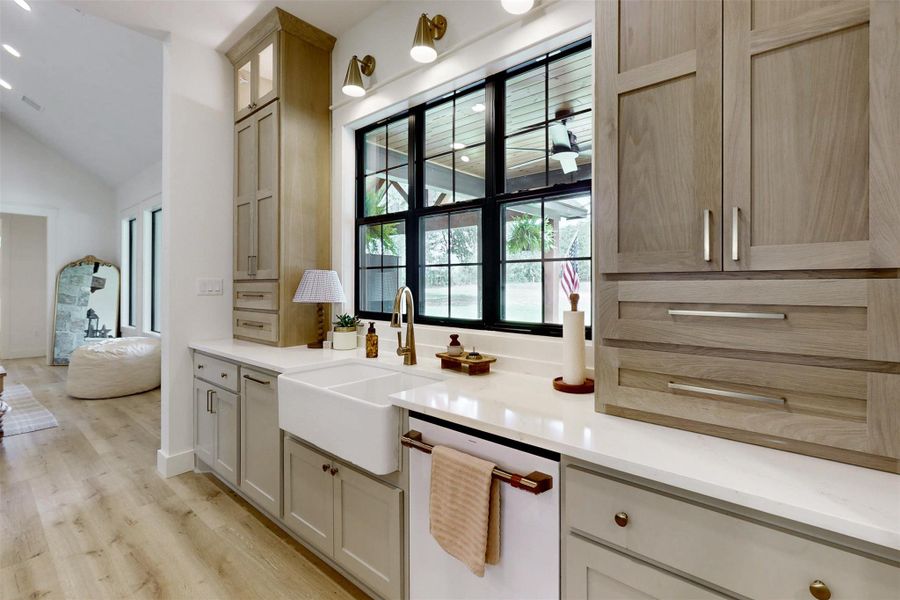Kitchen featuring dishwasher, light wood-style flooring, light countertops, lofted ceiling, and glass insert cabinets