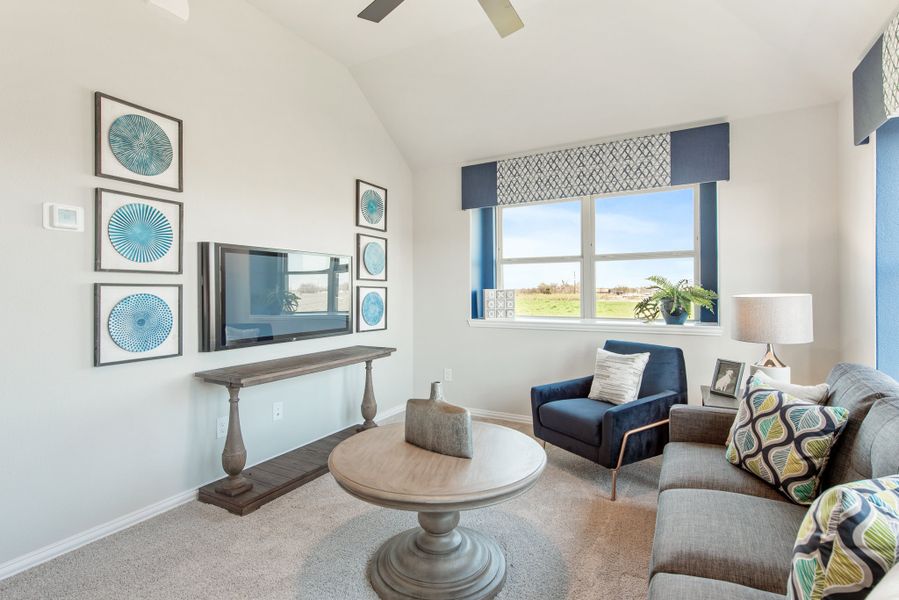 Living room with vaulted ceiling, wall-mounted TV, gray sofa, blue accent chair, and round coffee table on carpet