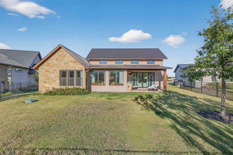 Back of property with a fenced backyard, a metal roof, a patio, and stone siding