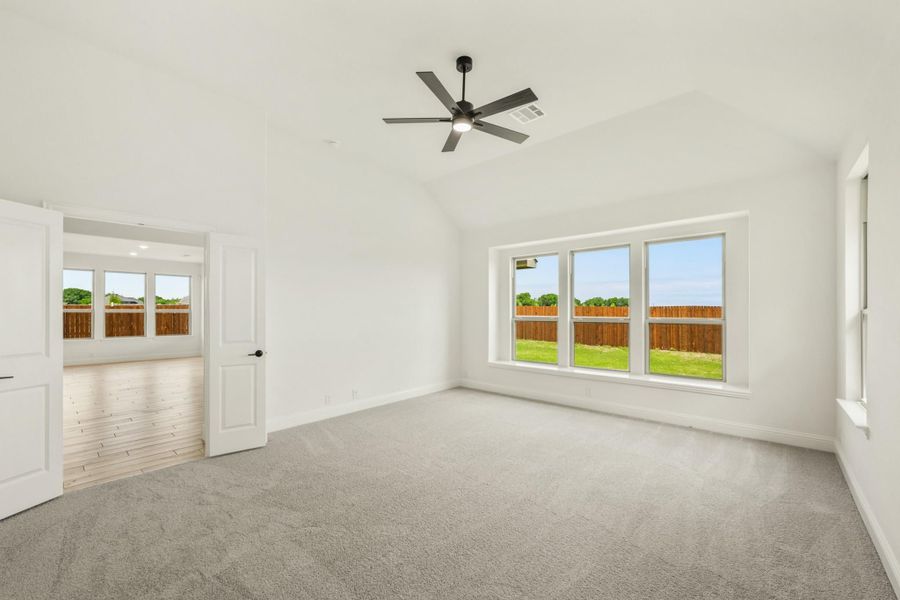 Empty bedroom with vaulted ceiling, ceiling fan, gray carpet, and large windows overlooking a backyard Empty bedroom with vaulted ceiling, ceiling fan, gray carpet, and large windows overlooking a backyard