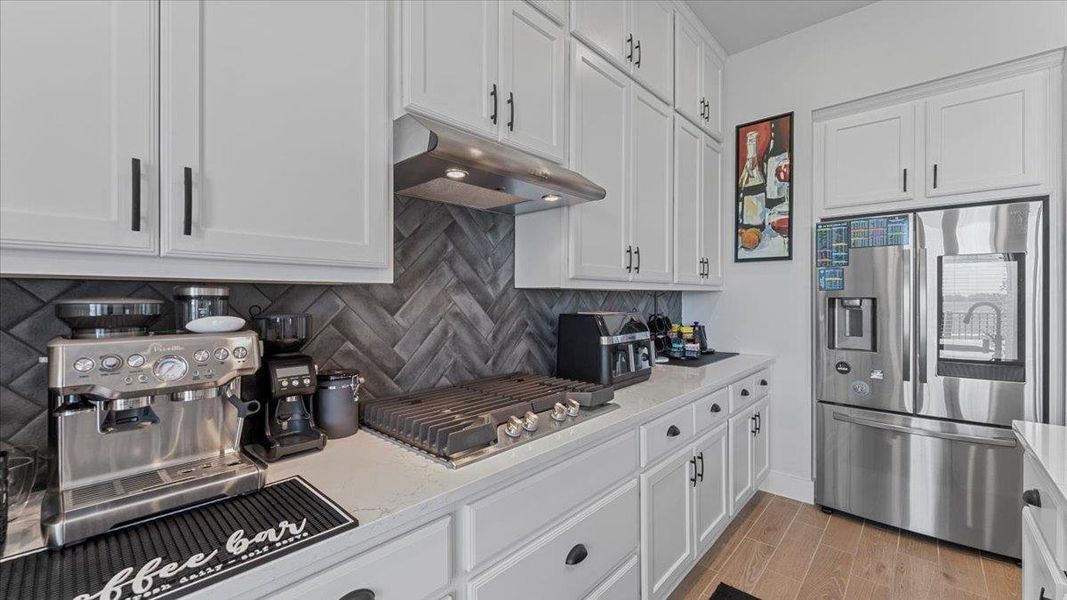 Kitchen featuring white cabinetry, appliances with stainless steel finishes, tasteful backsplash, wood tiled floors, and under cabinet range hood Kitchen featuring white cabinetry, appliances with stainless steel finishes, tasteful backsplash, wood tiled floors, and under cabinet range hood