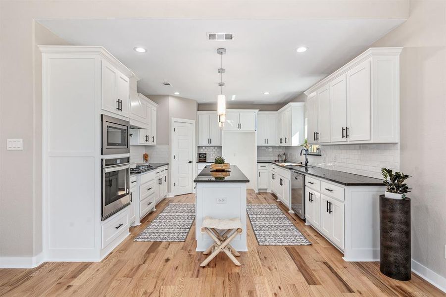 Kitchen featuring hanging light fixtures, white cabinetry, appliances with stainless steel finishes, a center island, and light wood-type flooring