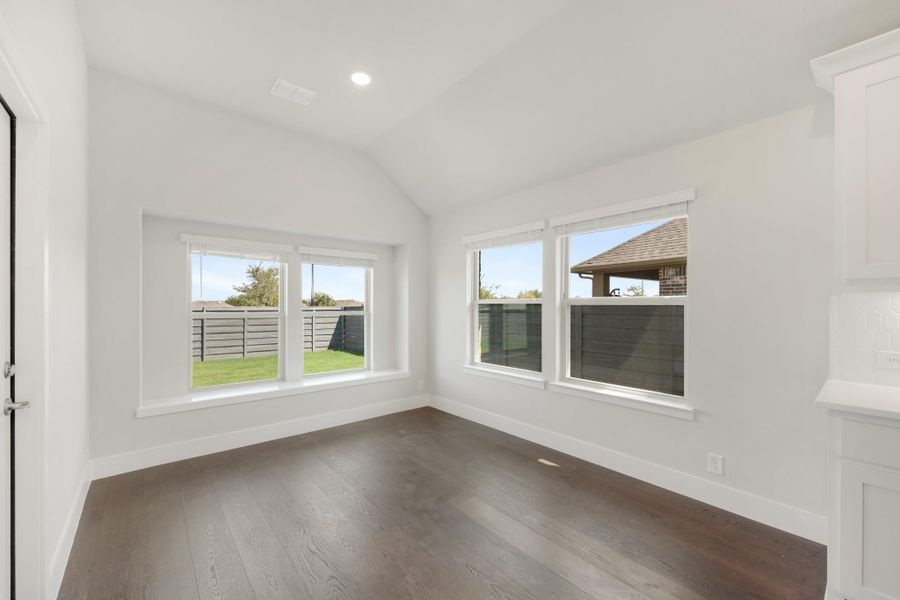Empty room with vaulted ceiling, dark hardwood floors, and multiple windows overlooking a fenced backyard Empty room with vaulted ceiling, dark hardwood floors, and multiple windows overlooking a fenced backyard
