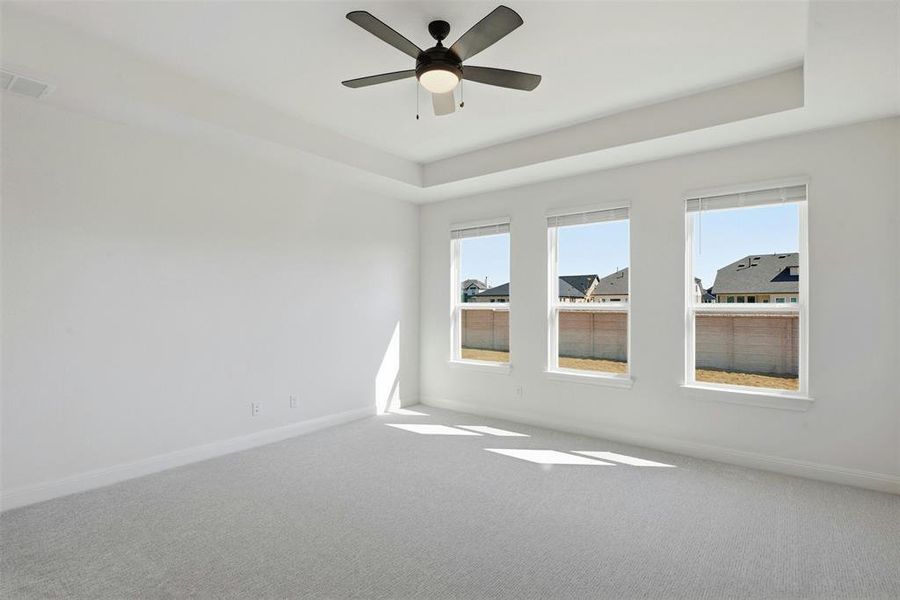 Room featuring three large windows with blinds, a tray ceiling, and a ceiling fan with integrated lighting
