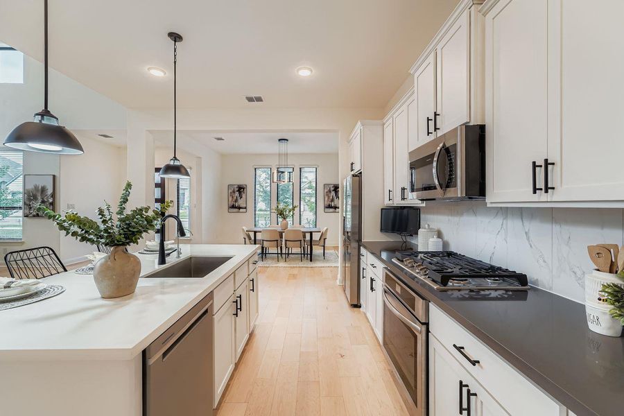 Kitchen with white cabinets, appliances with stainless steel finishes, decorative light fixtures, light wood-type flooring, and backsplash Kitchen with white cabinets, appliances with stainless steel finishes, decorative light fixtures, light wood-type flooring, and backsplash