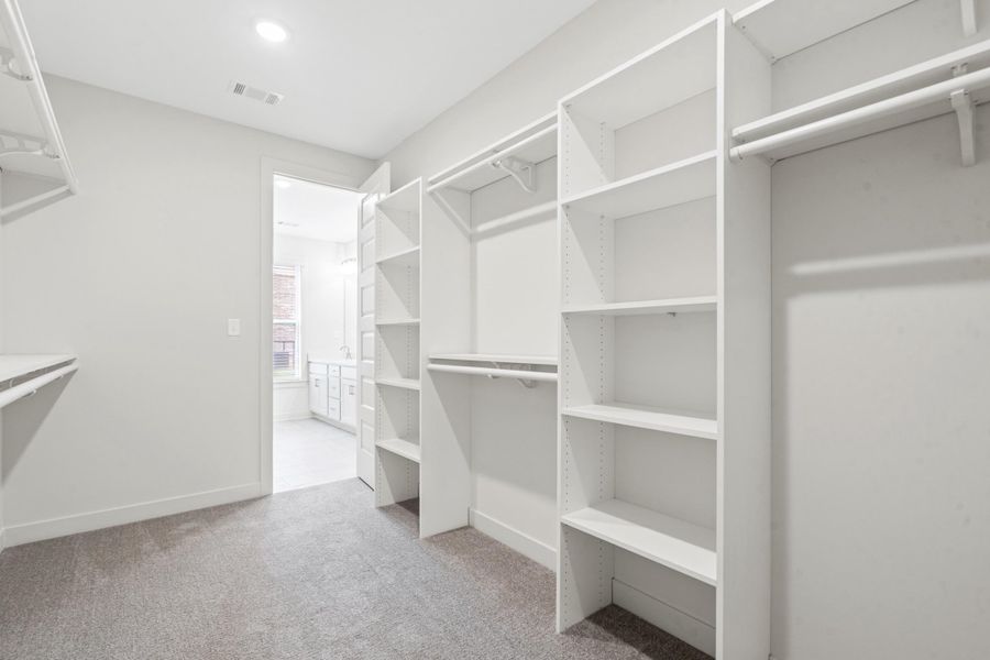 Spacious walk-in closet featuring light gray carpeting and custom white shelving Spacious walk-in closet featuring light gray carpeting and custom white shelving