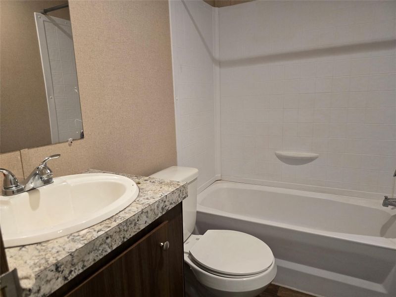 Full bathroom featuring a white tub, white tiled shower surround, integrated sink with chrome faucet, and a stone-finish countertop Full bathroom featuring a white tub, white tiled shower surround, integrated sink with chrome faucet, and a stone-finish countertop