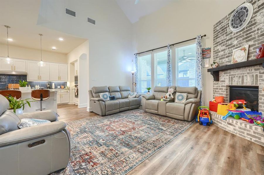 Living room with light hardwood / wood-style floors, a high ceiling, and a brick fireplace