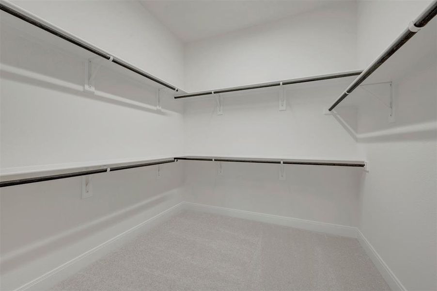 Spacious walk-in closet featuring light gray carpeting, white walls, multiple built-in shelving units, and metal hanging rods Spacious walk-in closet featuring light gray carpeting, white walls, multiple built-in shelving units, and metal hanging rods