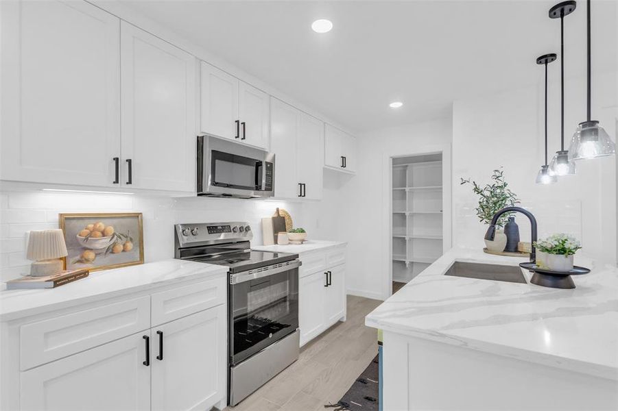 Kitchen featuring stainless steel appliances, white cabinets, light stone counters, recessed lighting, and hanging light fixtures
