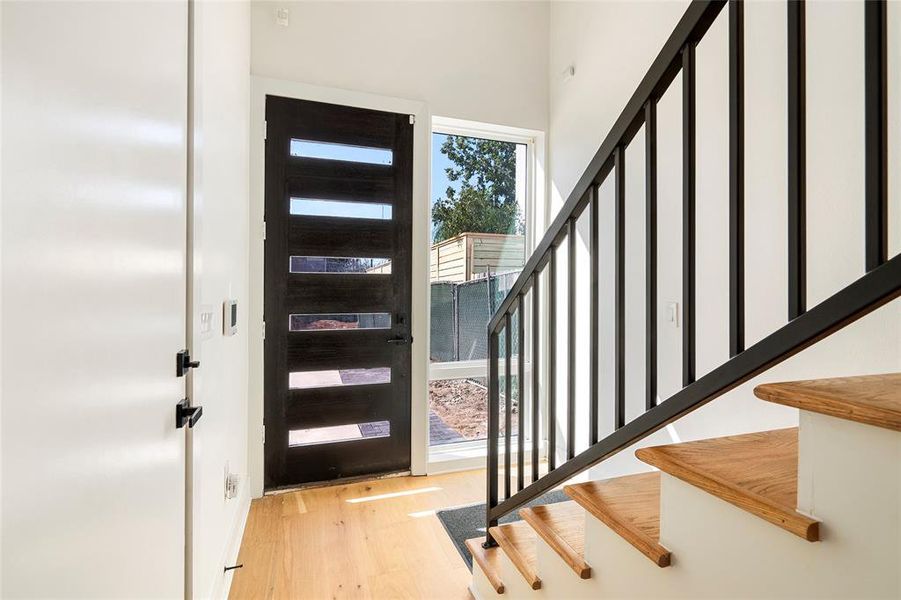 This photo showcases a bright, spacious open-concept living area with modern hardwood flooring, leading into a sleek kitchen with white cabinetry and stainless steel appliances. The room benefits from ample natural light and recessed lighting, ensuring a welcoming atmosphere.