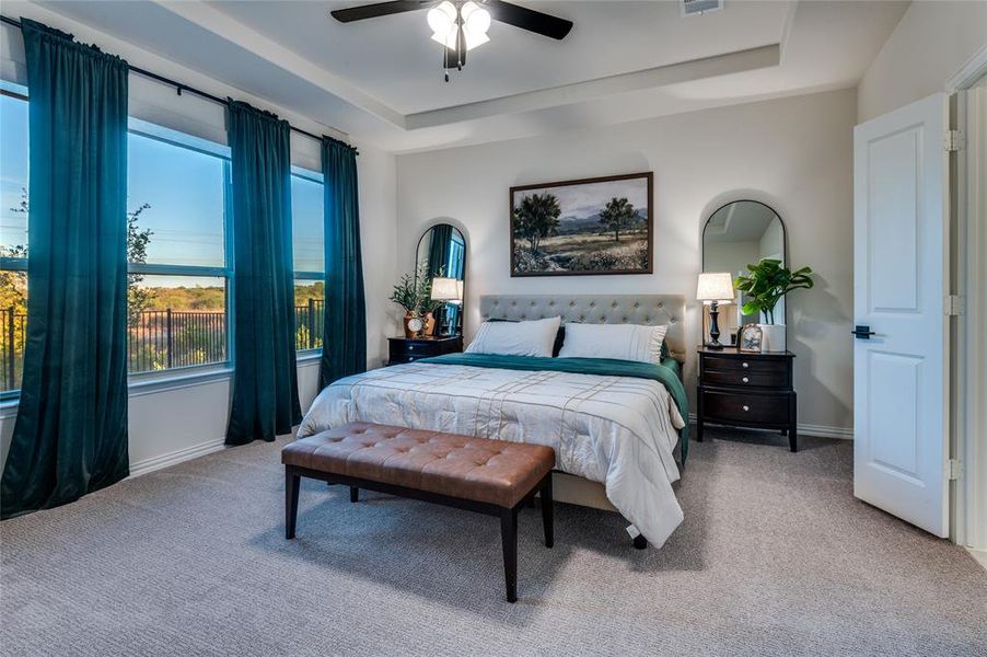 Bedroom with a raised ceiling, light carpet, and a ceiling fan
