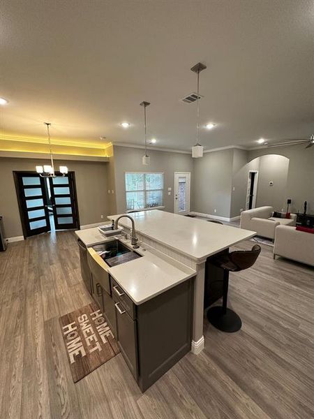 Kitchen with pendant lighting, open floor plan, a center island with sink, light wood finished floors, and ornamental molding