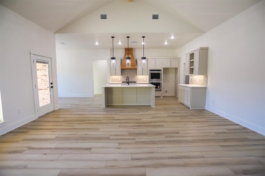 Kitchen with open floor plan, light countertops, a kitchen island with sink, hanging light fixtures, and tasteful backsplash
