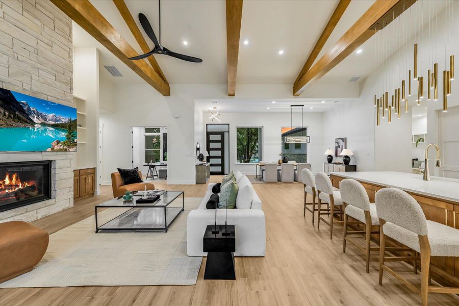 Living room featuring recessed lighting, light wood-type flooring, a stone fireplace, beamed ceiling, and ceiling fan