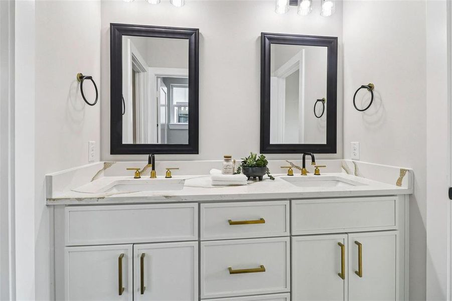 Bathroom vanity featuring dual sinks, white cabinetry with gold hardware, and two framed mirrors