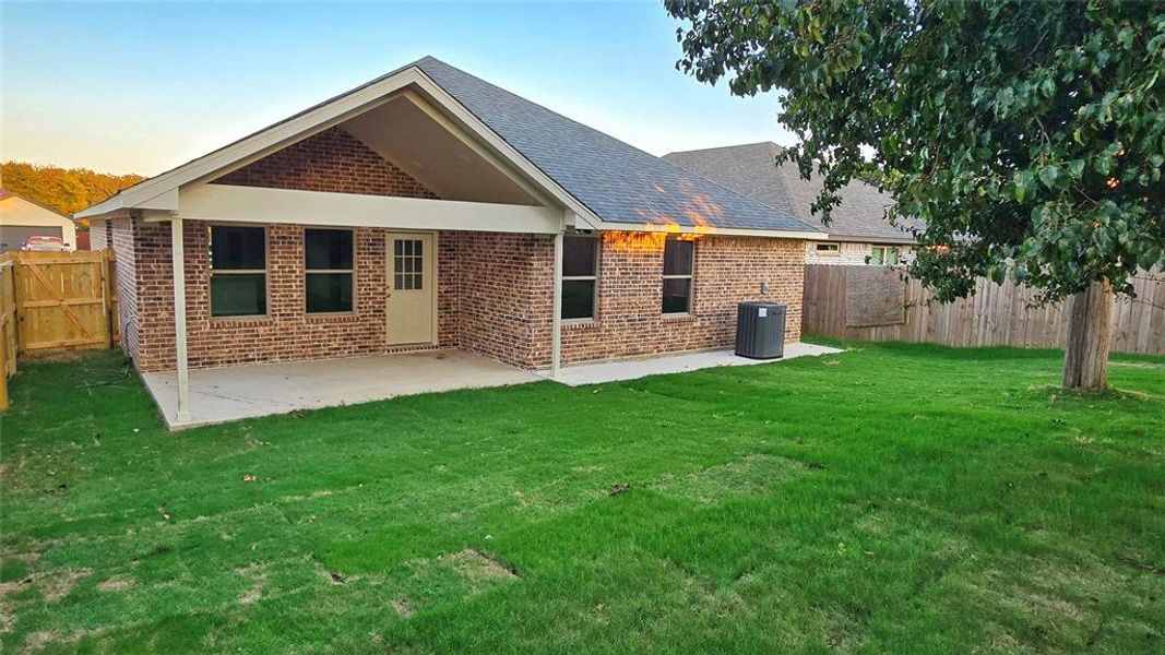 Rear view of property featuring brick siding, a fenced backyard, roof with shingles, and a patio